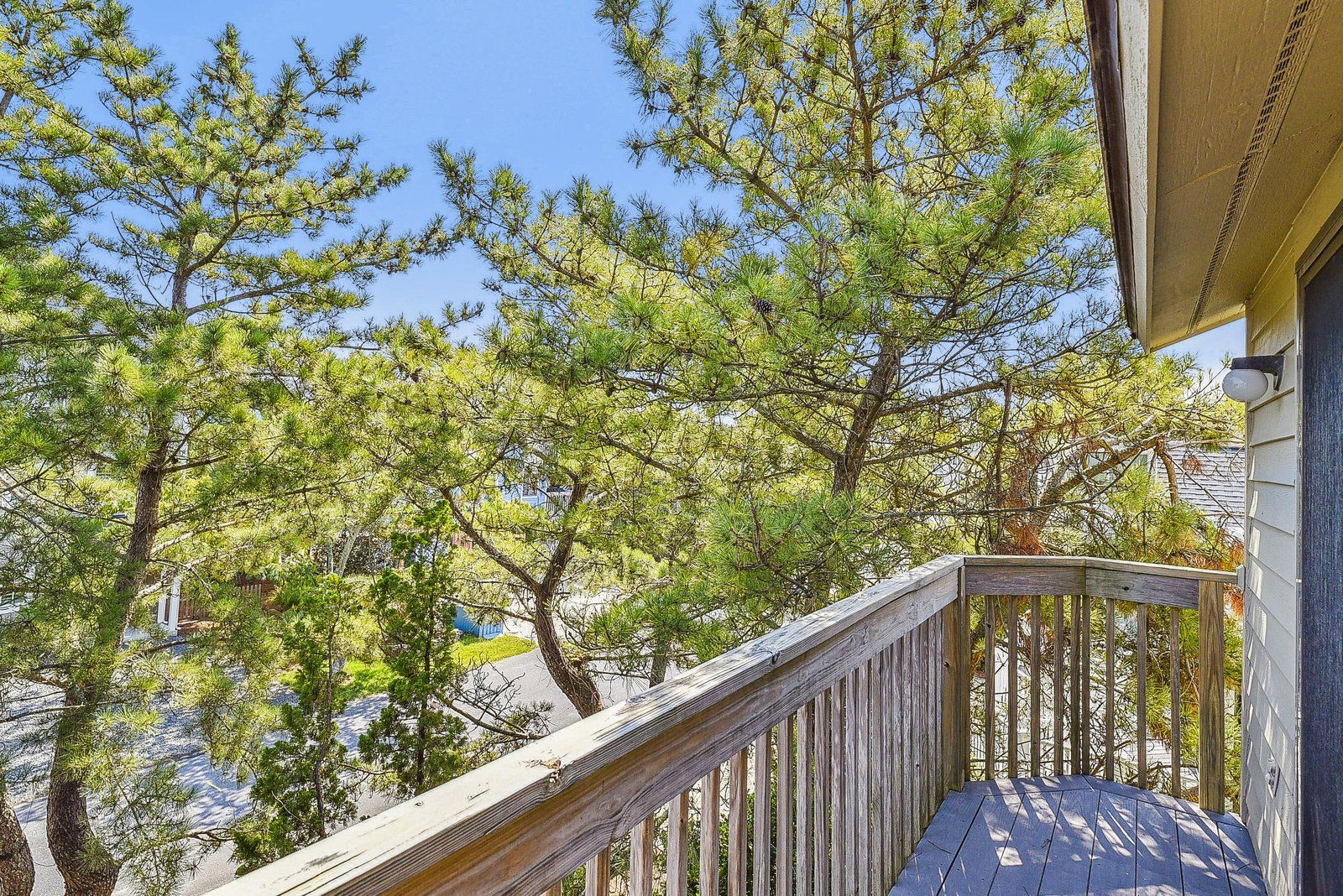 A wooden deck with a railing, overlooking a residential area with houses and trees.