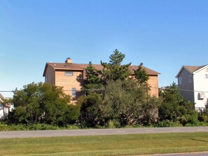 A two-story residential building with a brown exterior, surrounded by trees and a clear sky.