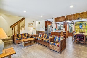 A spacious living area with a wooden staircase, a dining table with chairs, and a kitchen area with wooden cabinets.