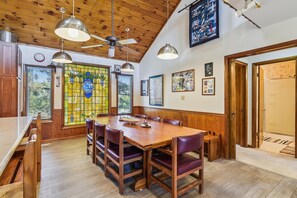 A dining area with a wooden table and chairs, a stained glass window, and a ceiling fan.