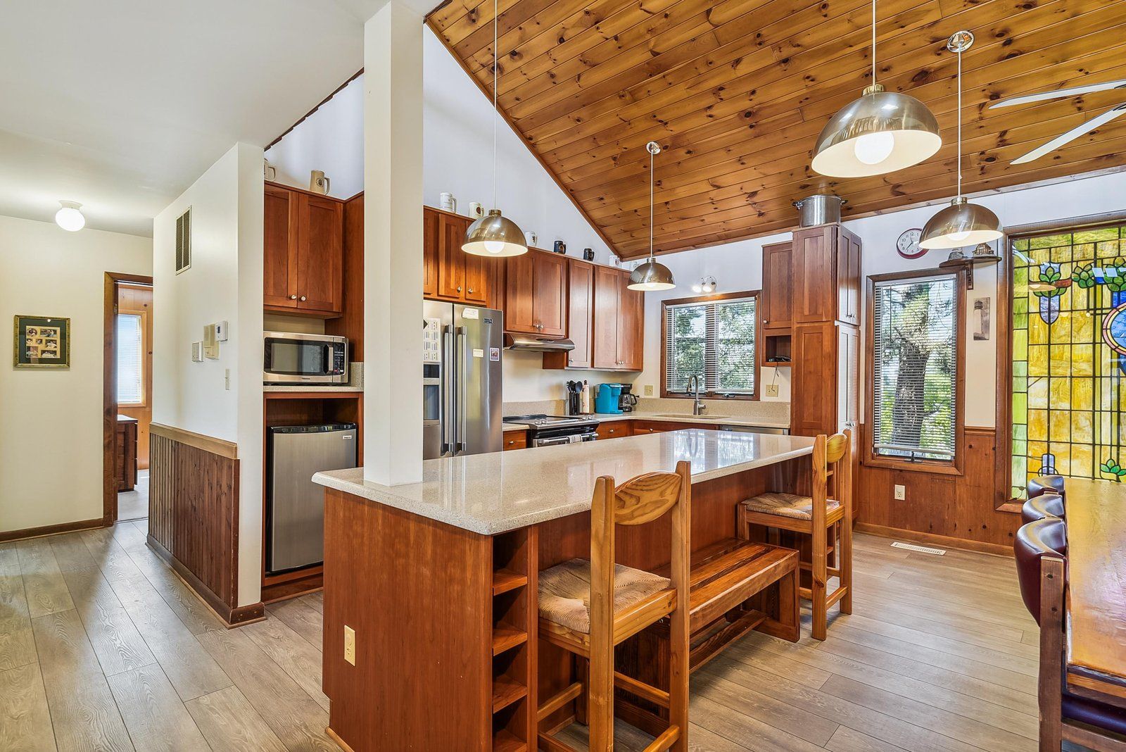 A kitchen with wooden cabinets, a stainless steel refrigerator, a microwave, and a large island with chairs.
