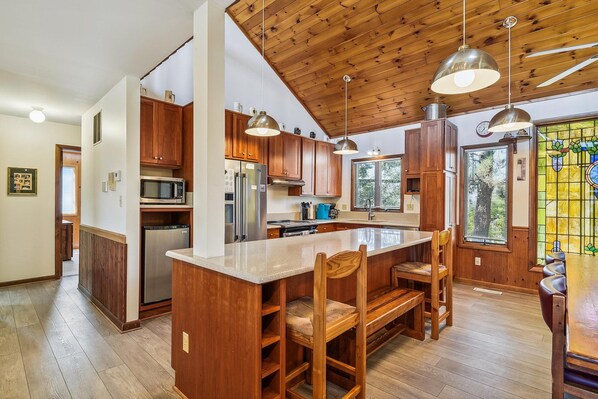 Una cocina con armarios de madera, un refrigerador de acero inoxidable, un microondas y una isla grande con sillas.