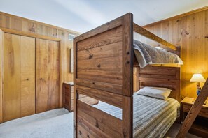 A bunk bed with a wooden headboard, a bedside table with a lamp, and a wardrobe in a wooden-paneled room. - Bethany Beach Coastal Retreat (South Bethany)