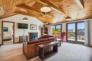 Amplia sala de estar con techo de madera, chimenea, televisor y un gran ventanal con vistas al exterior.
