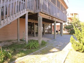A building with a covered outdoor area supported by wooden posts, a gravel path, and some greenery.