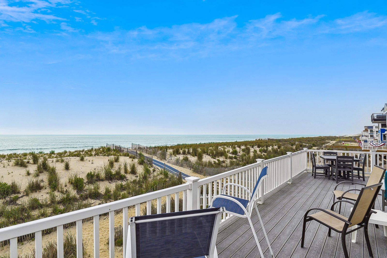 A deck with outdoor furniture overlooking a beach and ocean.