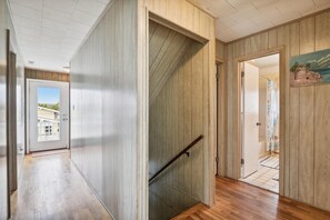 A hallway with wooden paneling, a glass door, and a staircase with a handrail. - The Buffer Zone: Oceanfront Bliss in Bethany Beach (South Bethany)