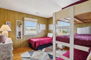 A room with bunk beds, wooden walls, a window with a view, and a patterned rug. - The Buffer Zone: Oceanfront Bliss in Bethany Beach (South Bethany)