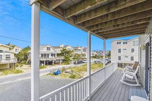 A wooden deck with a railing, overlooking a residential street with houses and parked cars. - The Buffer Zone: Oceanfront Bliss in Bethany Beach (South Bethany)