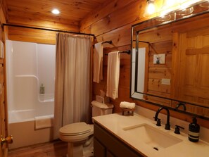 Un baño de cabaña de madera con bañera, inodoro, lavamanos y un espejo grande.