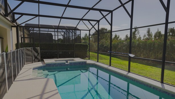 An indoor swimming pool with a glass ceiling, surrounded by a metal frame, and a view of a grassy area outside.