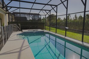 Una piscina interior con techo de vidrio, rodeada por una estructura metálica, y vistas a un área verde exterior.