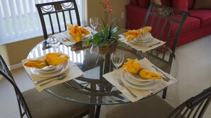 A dining table set for four with yellow napkins, a potted plant, and a red couch in the background.