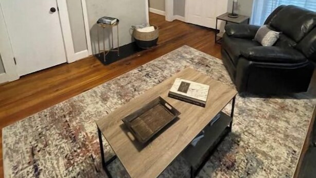 A living room with a ceiling fan, a flat-screen TV mounted above a fireplace, a black leather sofa, and a coffee table with a book. - Historic Mill House
 (Lexington)