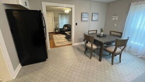 A compact living space with a dining area, a kitchen with a black refrigerator, and a hallway leading to a living room with a couch and a ceiling fan. - Historic Mill House
 (Lexington)