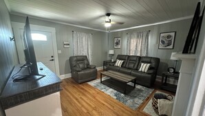 A living room with a sofa, armchairs, a coffee table, a TV, and a ceiling fan. - City Cottage Winston-Salem
 (Winston-Salem)