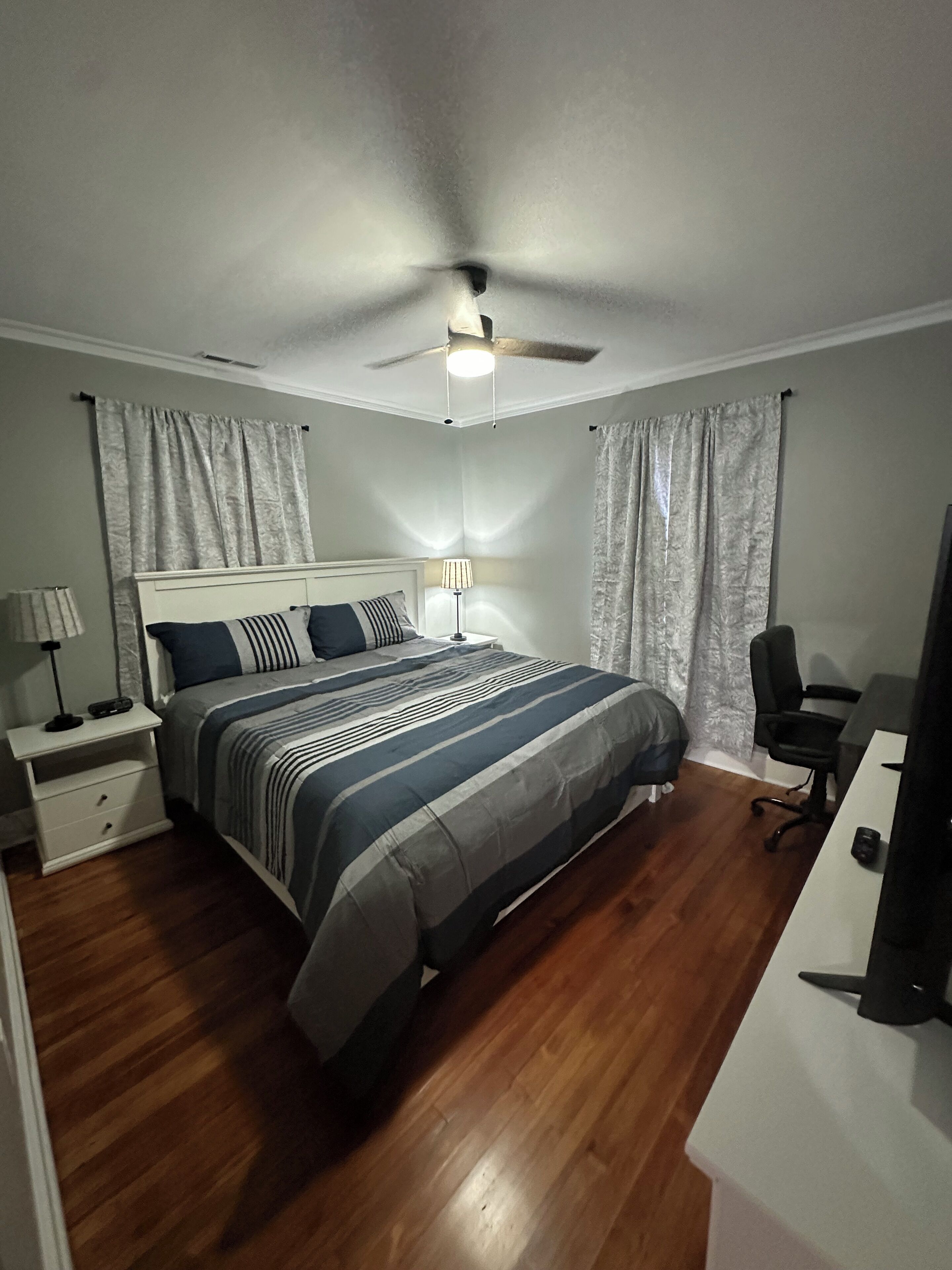 A bedroom with a bed, nightstand, desk, chair, and curtains.