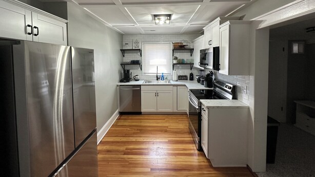 A modern kitchen with stainless steel appliances, white cabinetry, and a wooden floor. - City Cottage Winston-Salem
 (Winston-Salem)