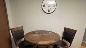 A dining area with a round wooden table and four chairs. A wall clock is mounted above the table. - Uptown Thomasville (Thomasville)