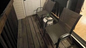 A covered porch with a white door, two chairs, a small table with a potted plant, and a window with blinds. - Uptown Thomasville (Thomasville)