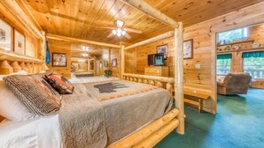 Ein Schlafzimmer in einer Blockhütte mit einem Bett, einem Schreibtisch, einem Sessel und einem Fernseher.