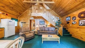 Ein gemütliches Blockhaus-Interieur mit einer Holztreppe, einem Essbereich und einem Wohnzimmer, möbliert mit Sofas und einem Couchtisch.