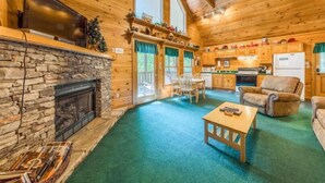 Ein gemütliches Blockhaus-Interieur mit Kamin aus Stein, Holzböden, Fernseher und Küchenzeile.