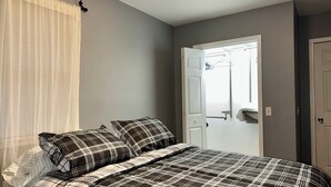 A bedroom with a bed, a window with curtains, a door, and a mirror.