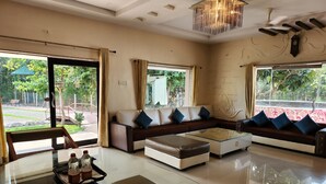 A modern living room with a glass coffee table, a sofa set, and a dining table with chairs. - Teakwood Farms (Wardha)