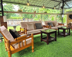 An outdoor seating area with wooden furniture and a green artificial grass floor. - Teakwood Farms (Wardha)