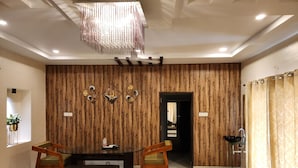 A modern dining area with a wooden accent wall, a chandelier, and a black dining table with two chairs. - Teakwood Farms (Wardha)