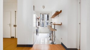 Un pasillo luminoso con suelo de madera, una lavadora y una zona de bar con taburetes.