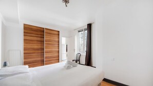 Una habitación de hotel moderna con una cama grande, un armario de madera, una ventana con cortinas y un radiador.