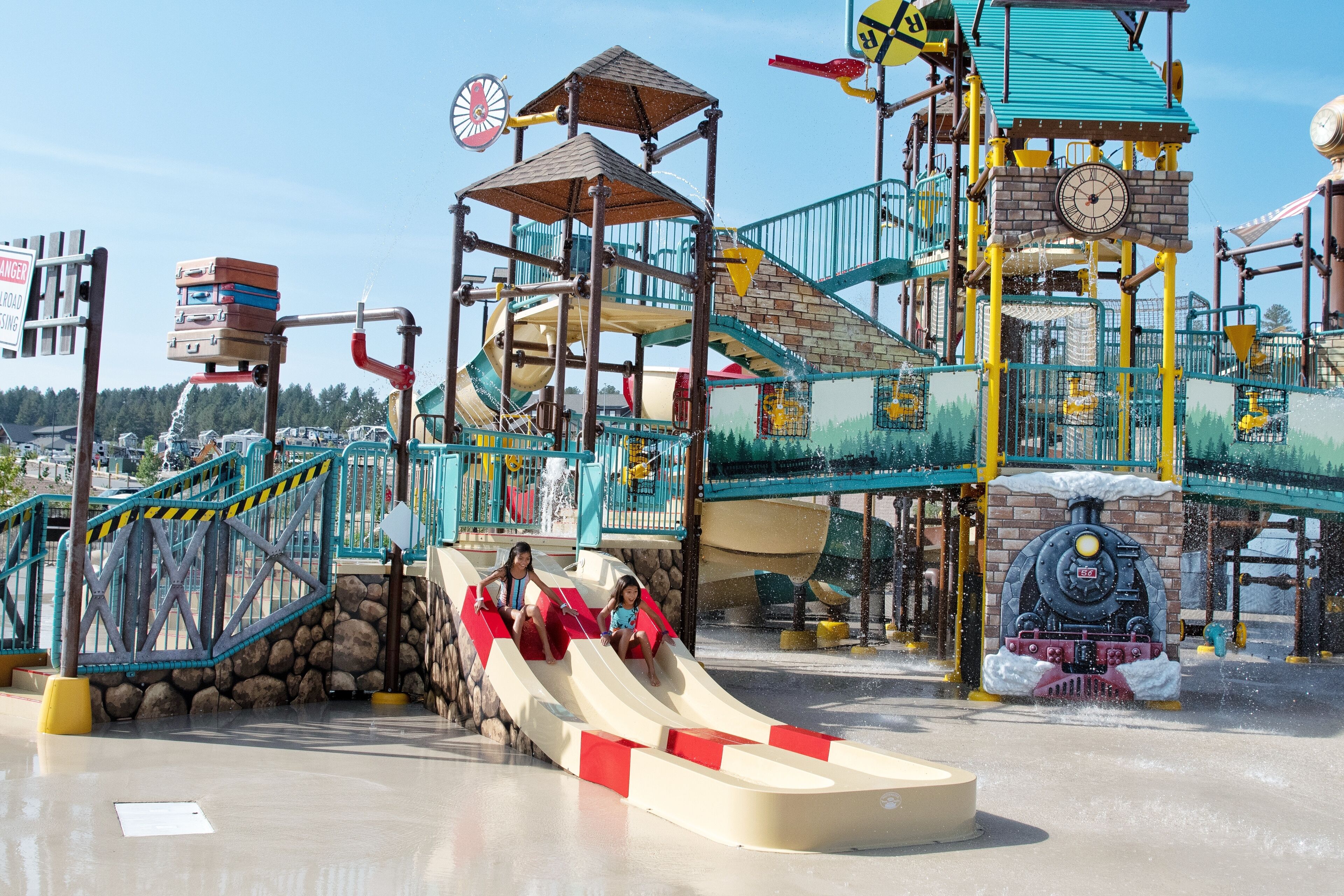 Un parque acuático con un tobogán, una torre del reloj y una estructura de juegos con temática de tren.