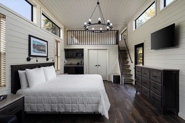 A bedroom with a large bed, a chandelier, a TV, and a staircase leading to an upper level.