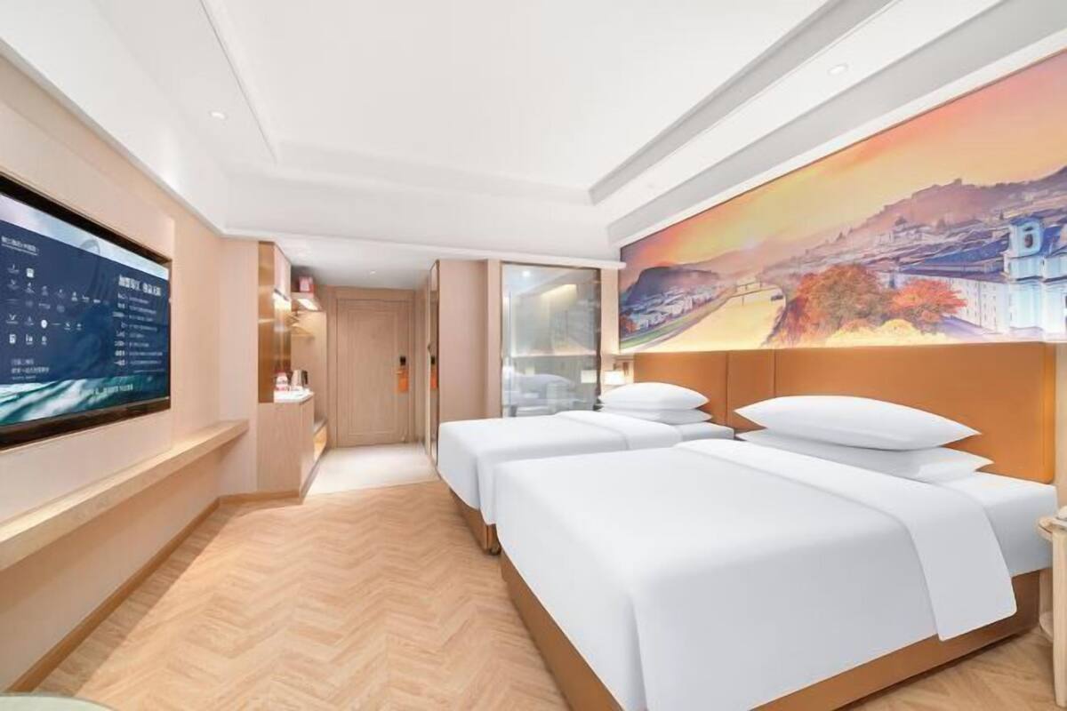 A hotel room with two beds, a TV, a painting, and a herringbone-patterned floor.