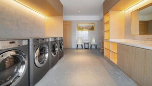 A modern laundry room with built-in washers and dryers, a small seating area with chairs, and a large mirror. - Vienna Hotel (Dongguan Houjie Avenue) (Dongguan)