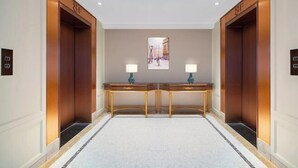A hallway with two elevators, a marble floor, and a table with two lamps. - Vienna Hotel (Dongguan Houjie Avenue) (Dongguan)