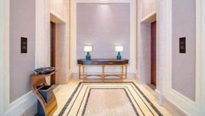 A hallway with a marble floor, a central console table with lamps, and two elevators. - Vienna Hotel (Dongguan Houjie Avenue) (Dongguan)