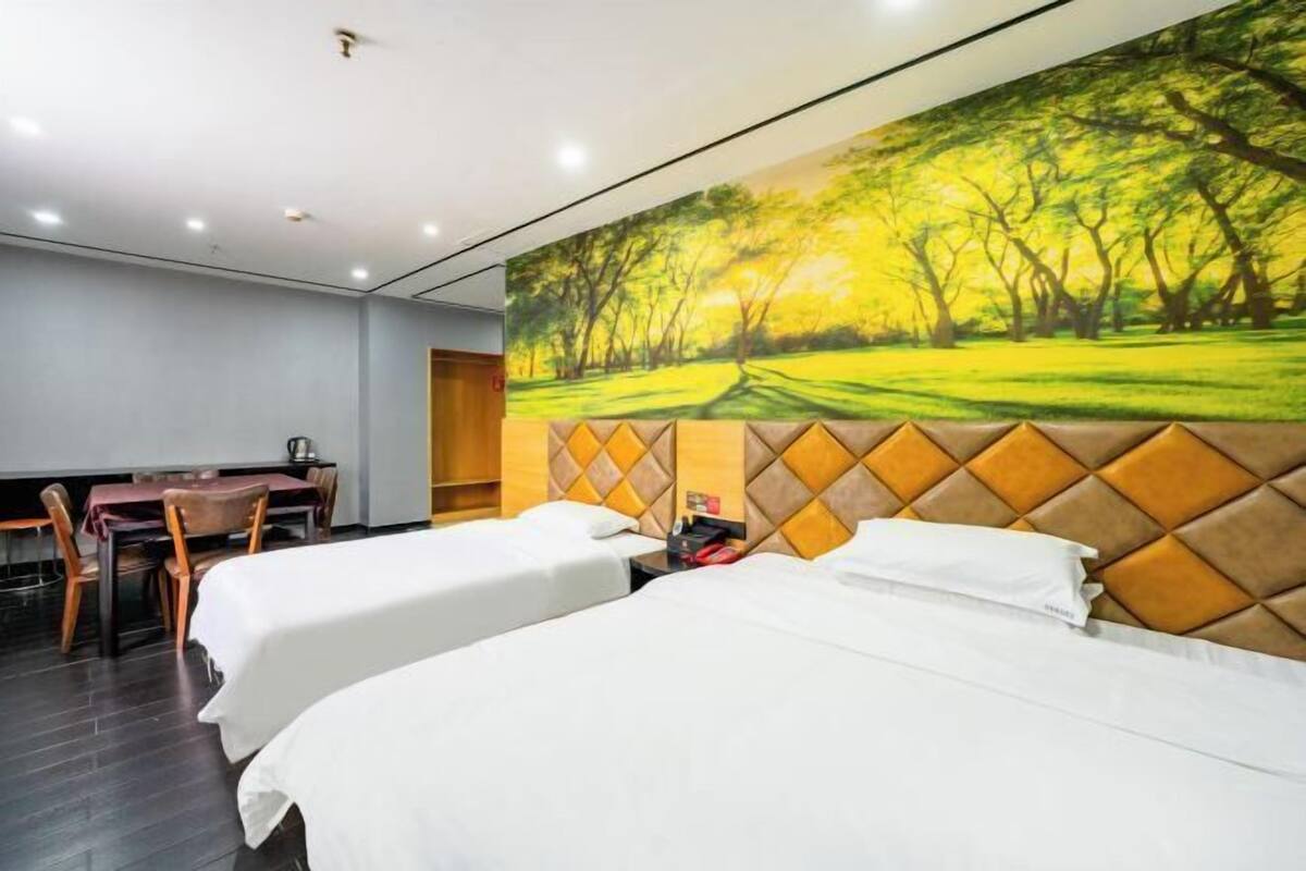 Une chambre d’hôtel avec deux lits, une table à manger et des chaises. Un grand tableau représentant une forêt est accroché au mur.