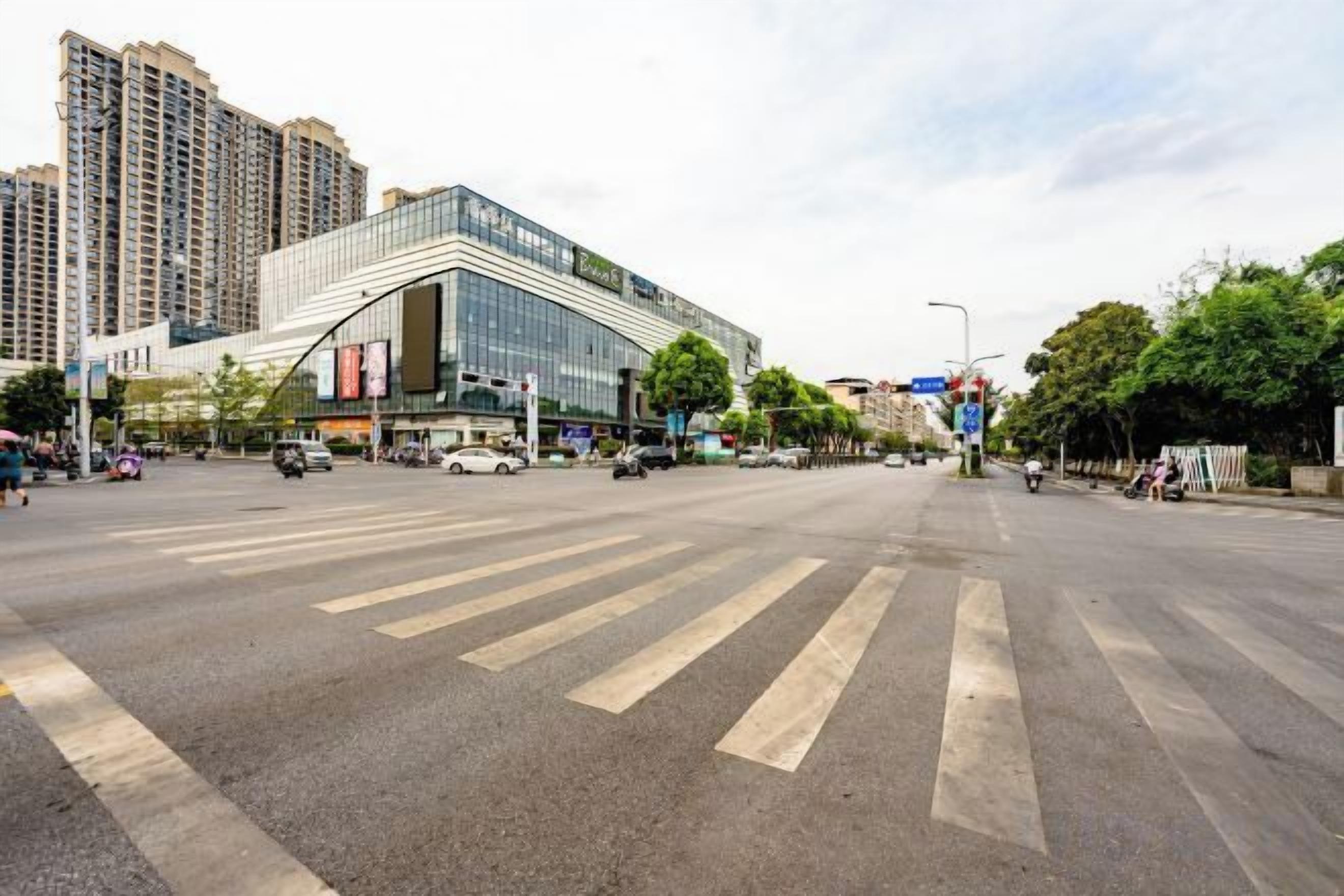 A wide street with a large building, crosswalks, and vehicles.