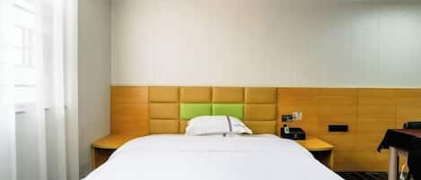 A hotel room with a bed, a wooden headboard, a bedside table, a nightstand, and a small table with a chair.
