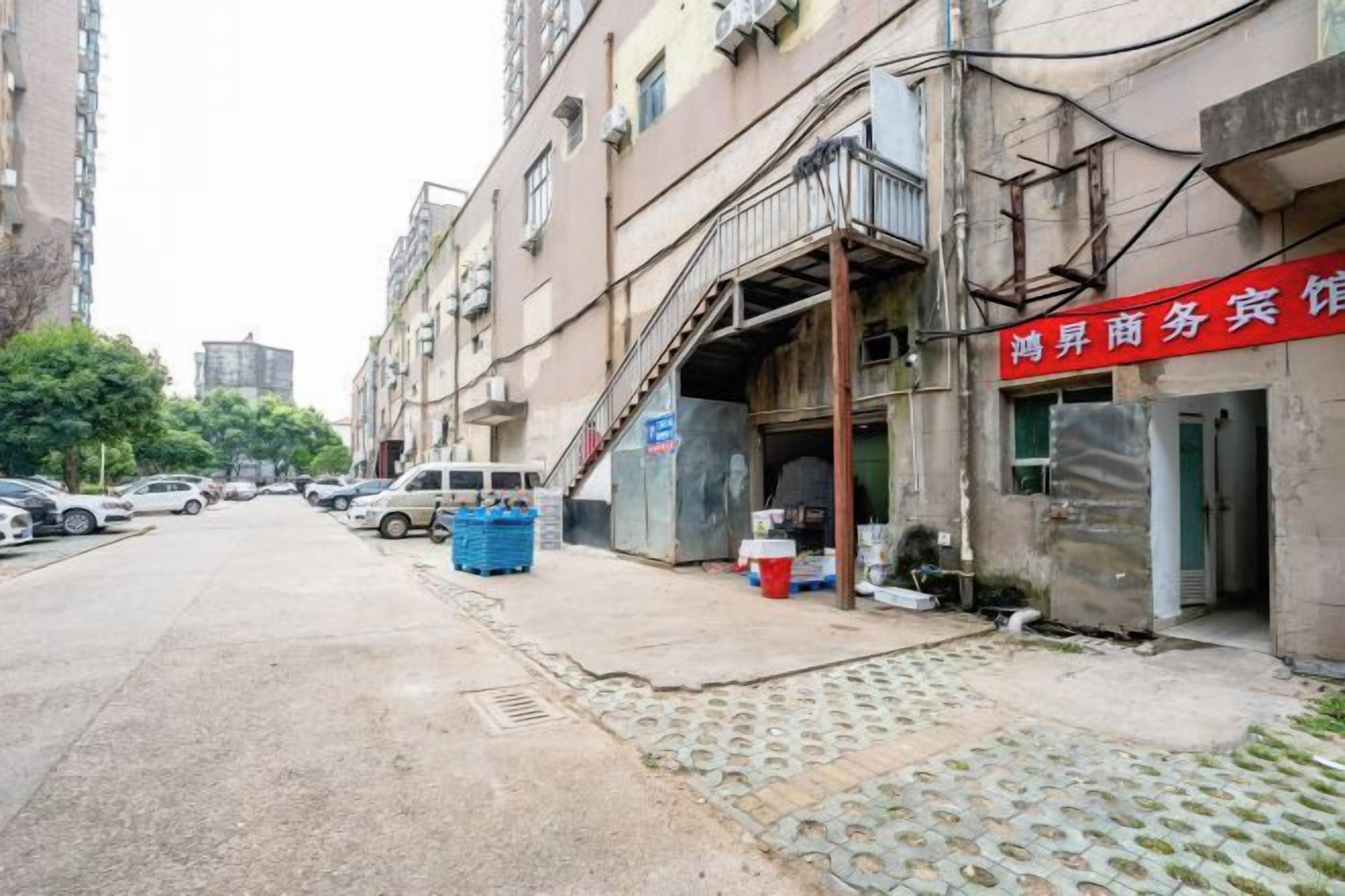 Une vue de rue avec un immeuble orné d’une enseigne rouge, d’une échelle de secours et de voitures garées.