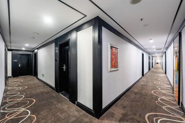 A hotel corridor with doors, a patterned carpet, and a framed picture on the wall. - Hongsheng Business Hotel (Nanchang)