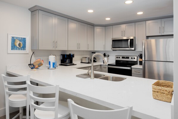 A modern kitchen with white cabinetry, stainless steel appliances, and a white marble countertop. - All New! Gulf Front! High End! Pelicans Roost 105 on Sanibel Island (Sanibel)