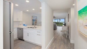 A modern kitchen with white cabinets, a dishwasher, and a view to the outside.
