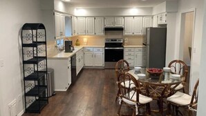 A compact kitchen with white cabinets, a black oven, and a dining area with wicker chairs and a glass table. - The Castle at Camorene

 (Springfield)