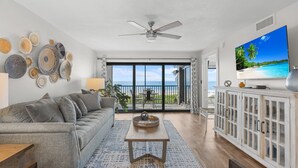 Un salon avec un canapé, une table basse et un téléviseur. Il y a un balcon avec vue sur l’océan.