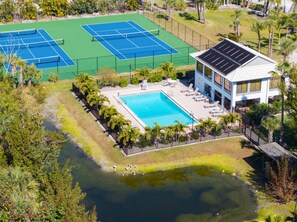 An aerial view of a property with two tennis courts, a swimming pool, and a building with solar panels.