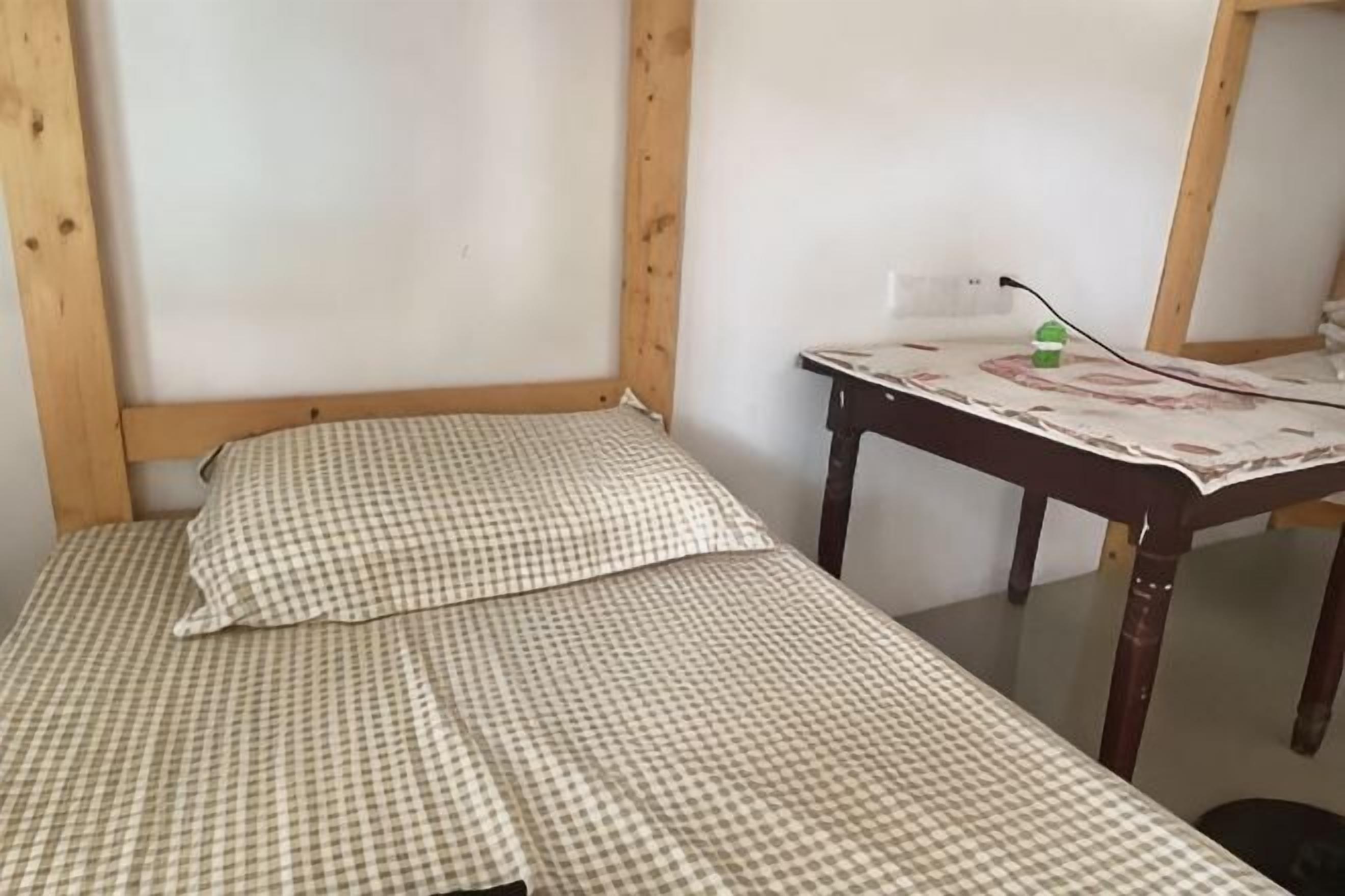 Una stanza con una coperta a quadri, una testata del letto in legno, un tavolo con una tovaglia decorata e uno specchio appeso al muro.